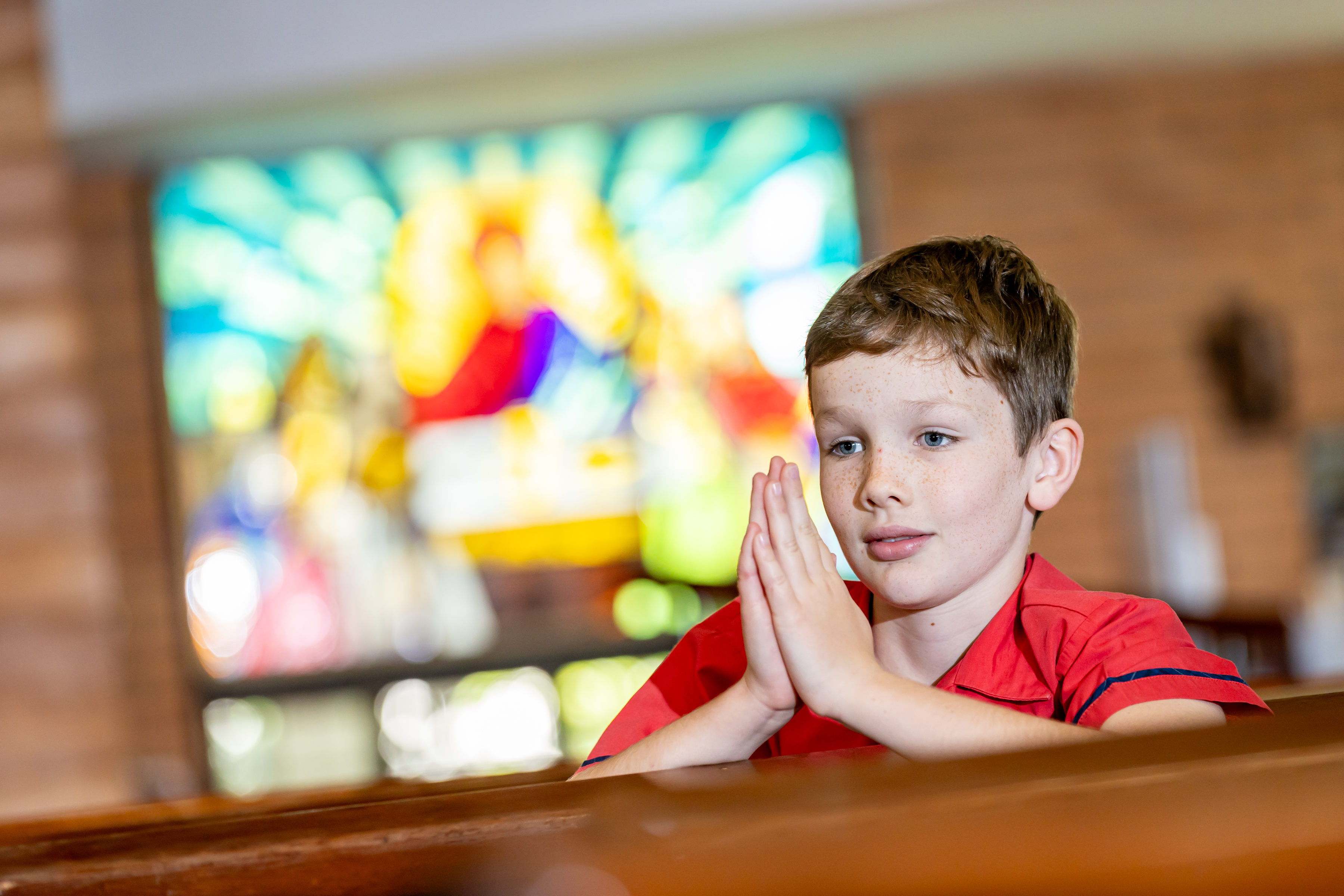 Student in school uniform praying in a church setting reflecting faith formation and spiritual life within the school community